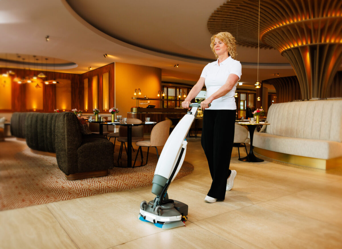 Vrouw gebruikt een i-mop schrobzuigmachine om de vloer in de lobby van een hotel schoon te maken
