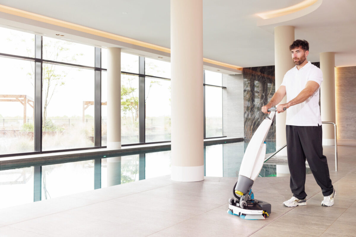 Man gebruikt een i-mop schrobzuigmachine om de vloer rondom een zwembad schoon te maken