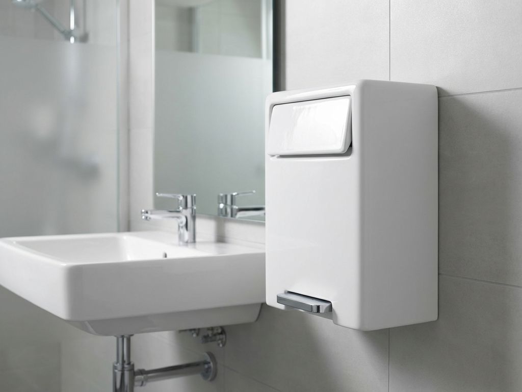 Witte keramische hygiƫne-afvalbak met voetpedaal gemonteerd naast moderne wastafel in schone badkamer