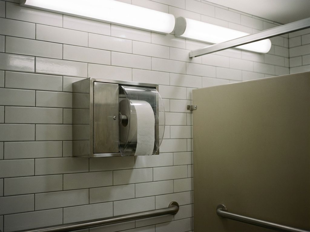 Schone kantoortoiletcabine met chromen toiletpapier dispenser op witte tegelmuur, gevuld met verse rol